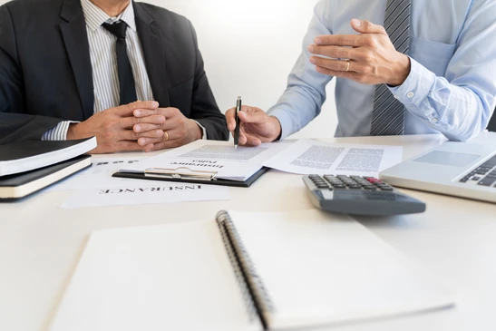 Deux hommes d'affaires en costume et cravate assis à une table de réunion, l'un signant des documents contractuels