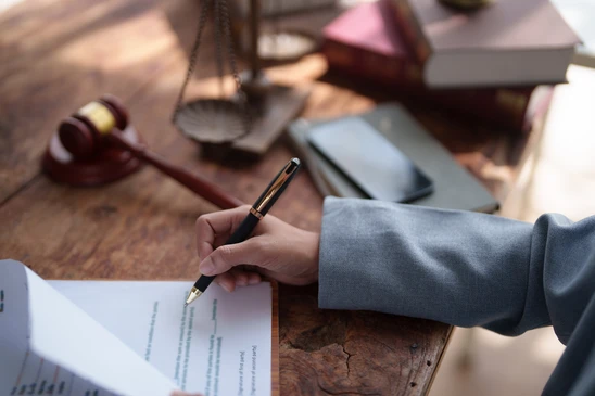 Un professionnel en costume sombre travaille à son bureau, rédigeant des documents juridiques avec un stylo plume