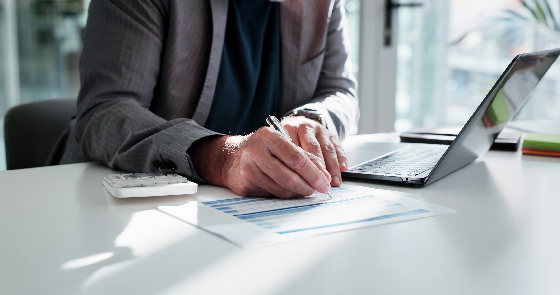 Un professionnel en costume sombre travaille à son bureau, rédigeant des documents juridiques avec un stylo plume
